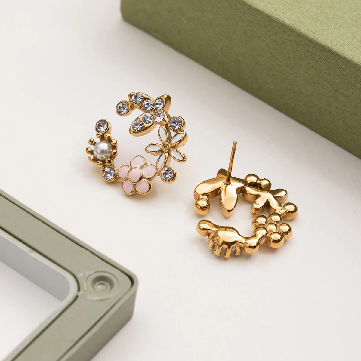 Gold earrings with floral and pearl designs on a light surface.