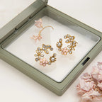 Gold floral earrings in a jewelry box with pink flowers on a white background
