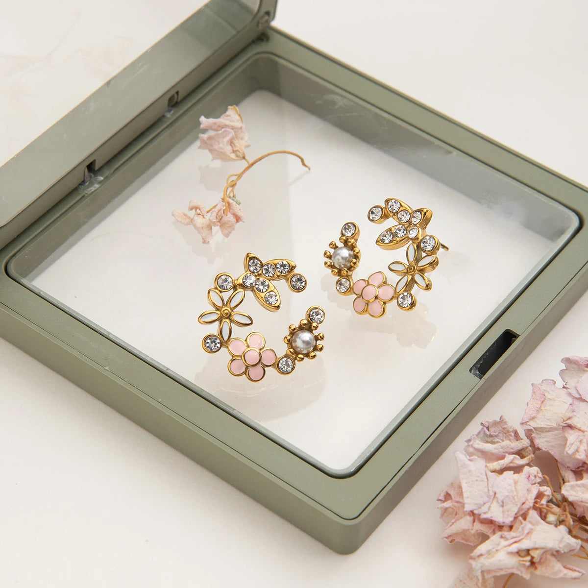 Gold floral earrings in a jewelry box with pink flowers on a white background