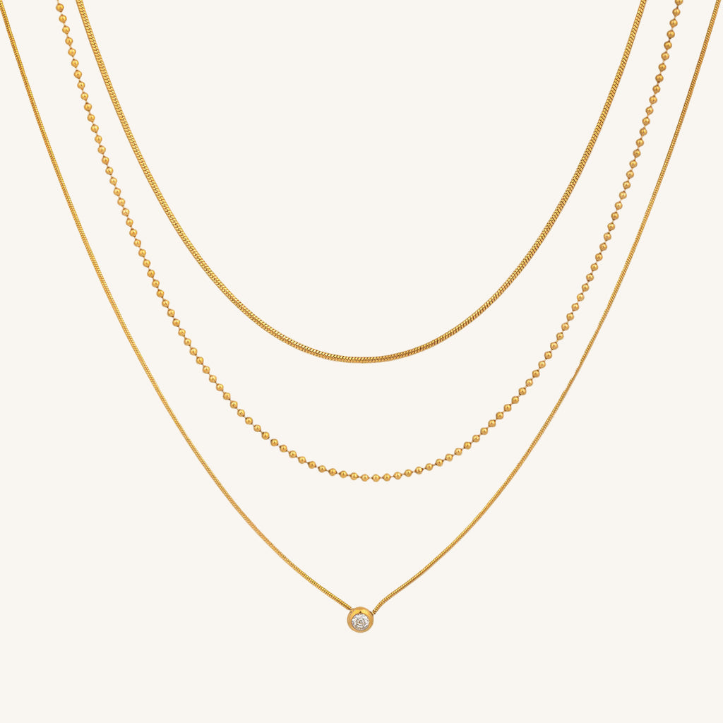 Three gold necklaces on a beige background
