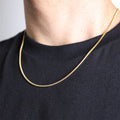 Gold chain necklace worn by a person on a plain background