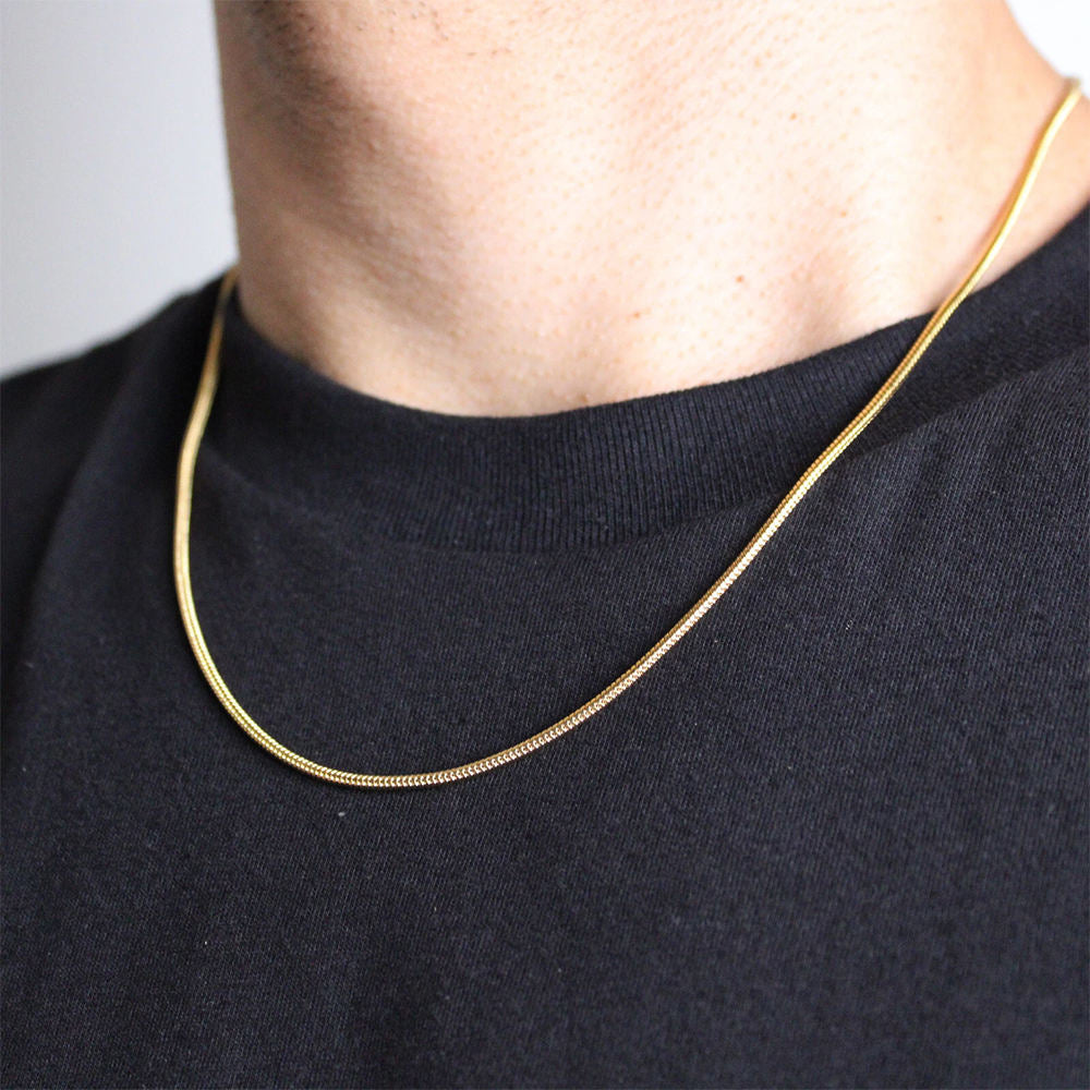 Gold chain necklace worn by a person on a plain background