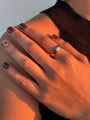 Close-up of a hand wearing a gold ring with a diamond on a neutral background