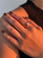 Close-up of a hand wearing a gold ring with a diamond on a neutral background