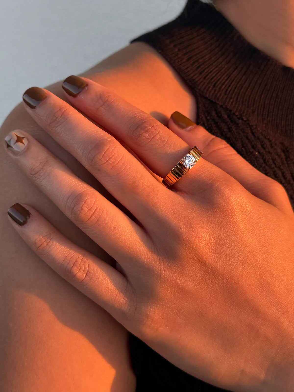 Close-up of a hand wearing a gold ring with a diamond on a neutral background