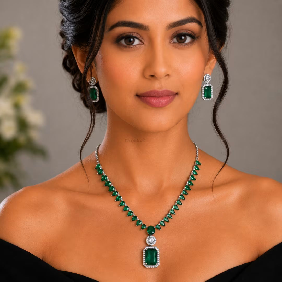 Woman wearing a green emerald necklace and earrings against a neutral background