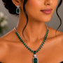 Woman wearing a green emerald necklace and earrings with a blurred background
