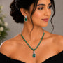 Woman wearing a green emerald necklace and earrings against a neutral background