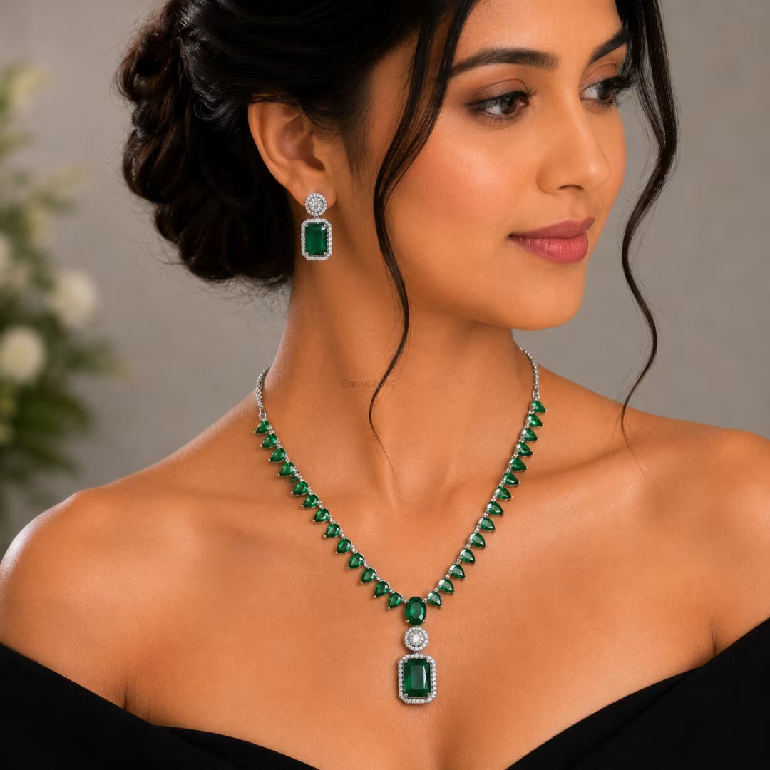 Woman wearing a green emerald necklace and earrings against a neutral background