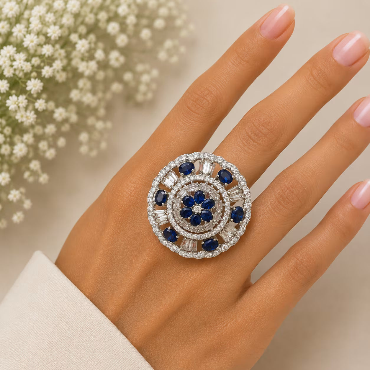 Close-up of a hand wearing a decorative ring with blue stones and white accents, against a neutral background.