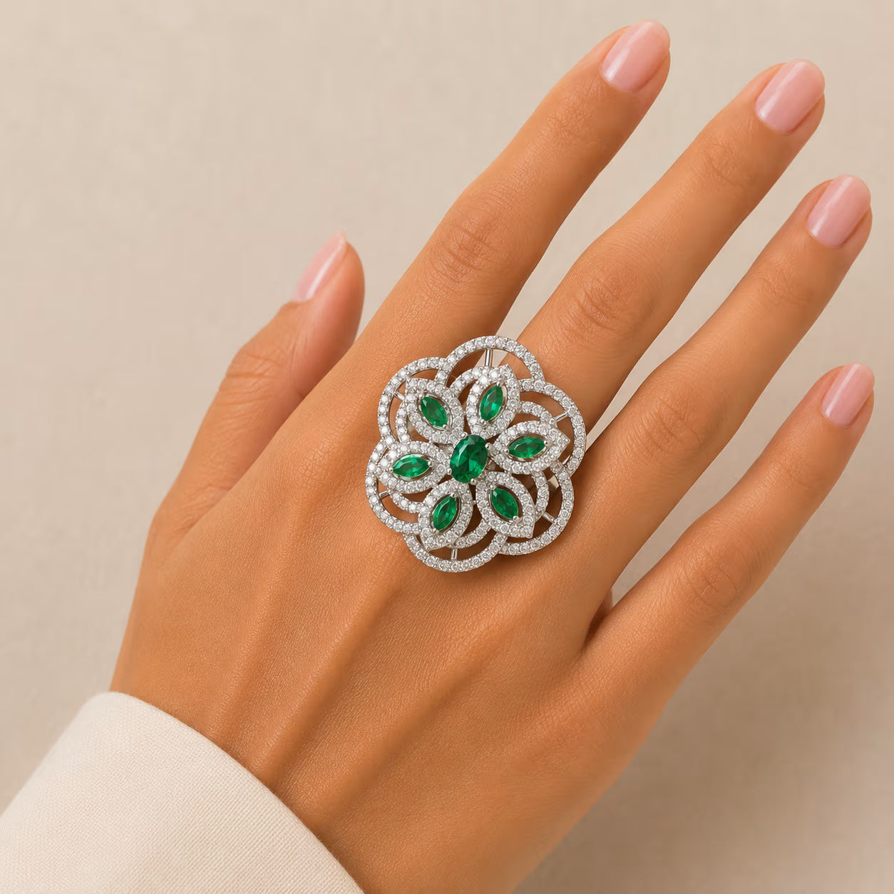 Elegant ring with green gemstones on a hand against a beige background