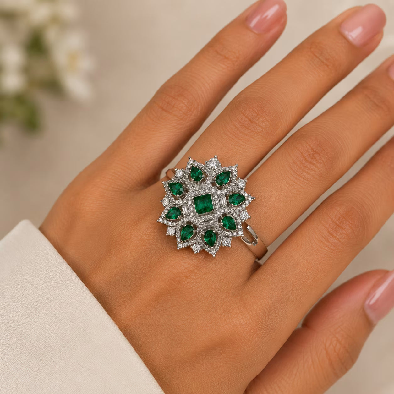 Close-up of a hand wearing a decorative ring with green gemstones and clear stones.