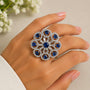 Silver ring with blue gemstones on a hand against a neutral background