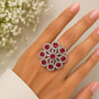Hand wearing a ring with red gemstones against a neutral background