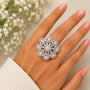 Silver floral ring on a hand with a blurred background of white flowers