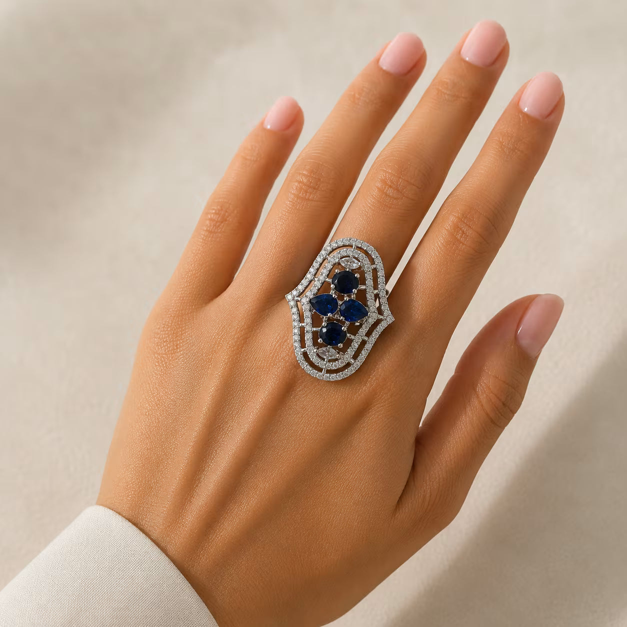 Hand wearing a decorative ring with blue stones on a neutral background