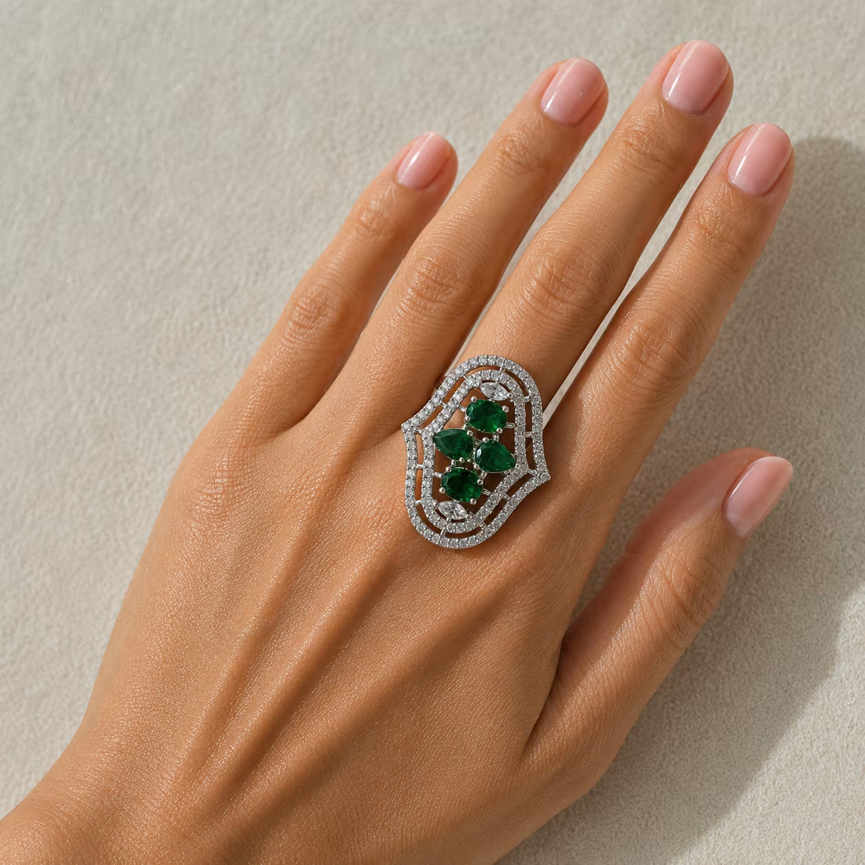Hand wearing a decorative ring with green gemstones on a neutral background