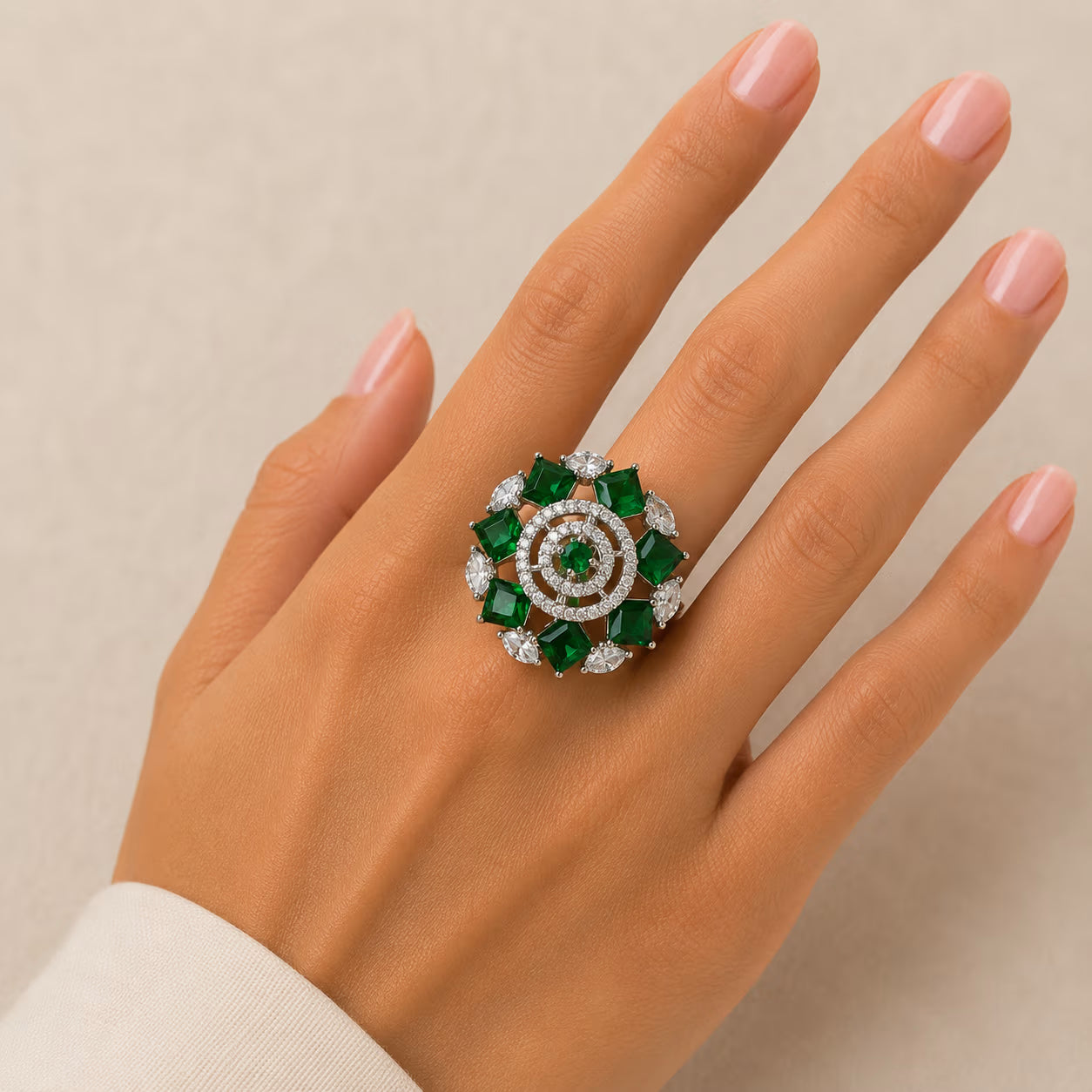 Ring with green gemstones and diamonds on a hand against a beige background