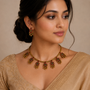 Woman wearing a gold necklace with green and red stones against a beige background