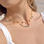 Close-up of a woman wearing a colorful gemstone necklace on a plain background