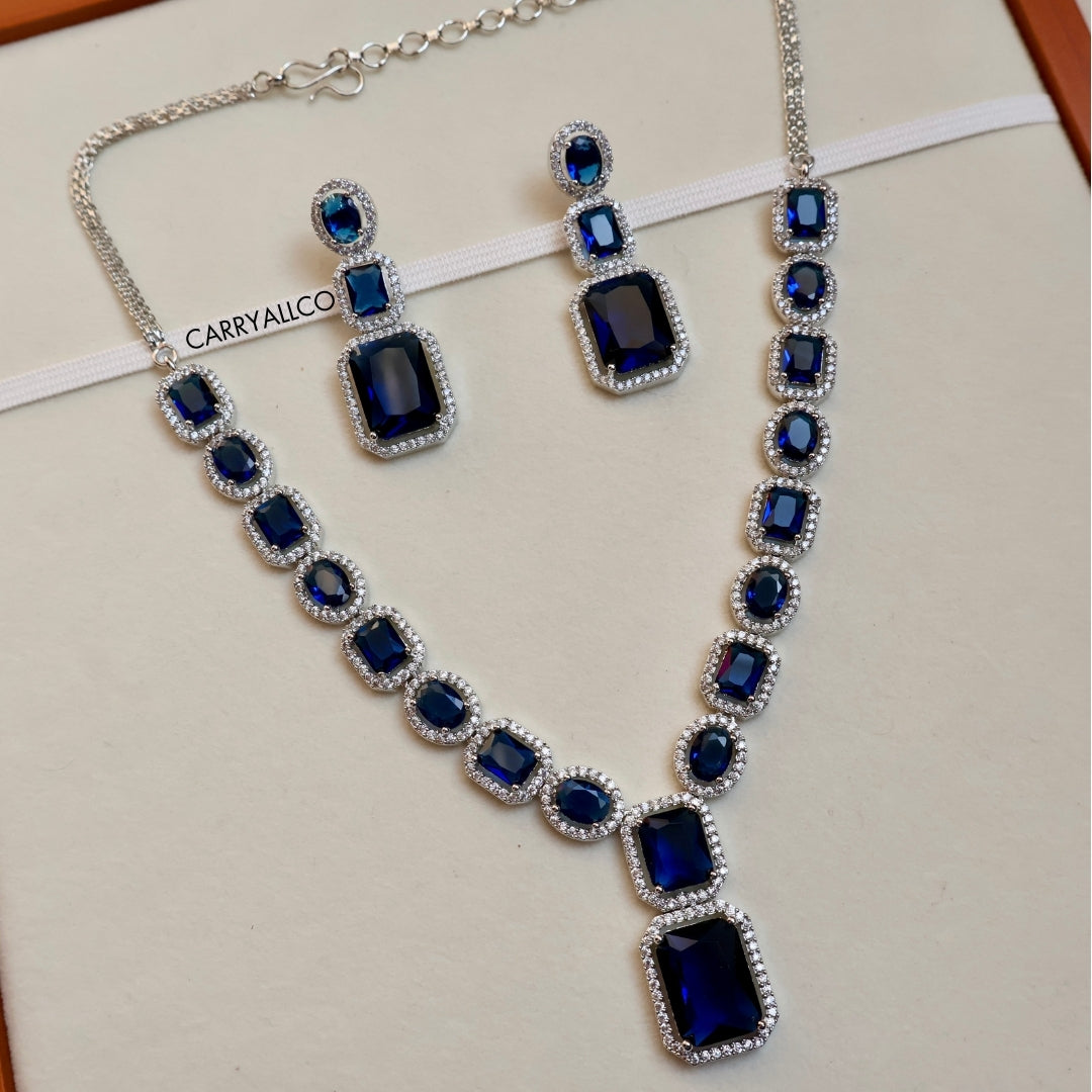 Jewelry set with necklace and earrings featuring blue gemstones on a white background.
