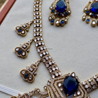Gold necklace with blue gemstones on a light gray background