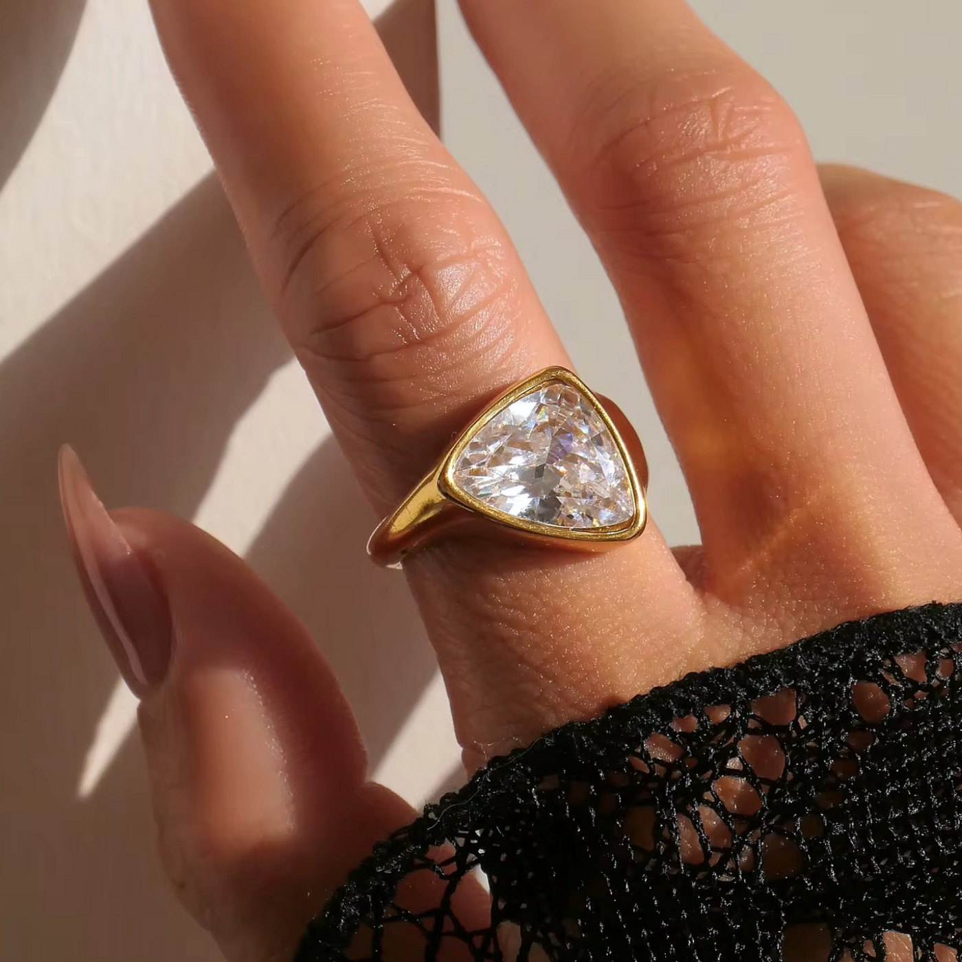 Hand wearing a gold ring with a large diamond on a neutral background