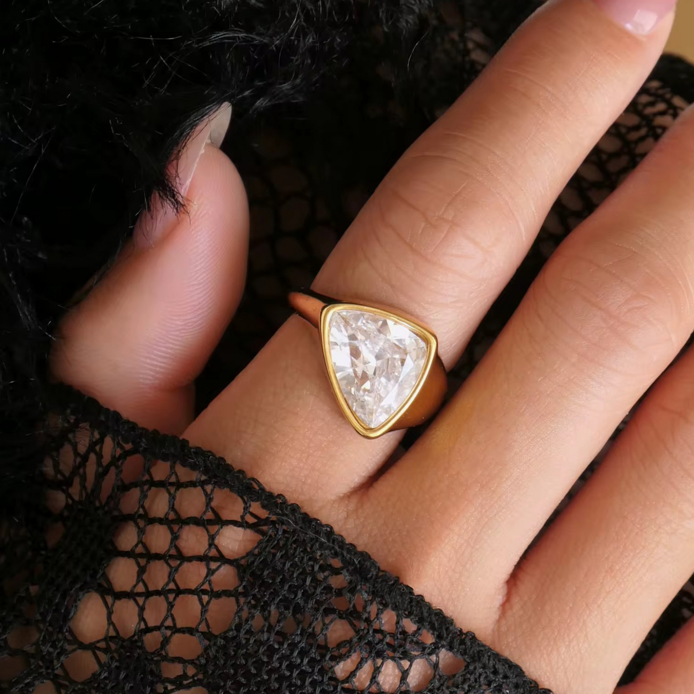 Gold ring with a triangular gemstone on a hand wearing black lace gloves.