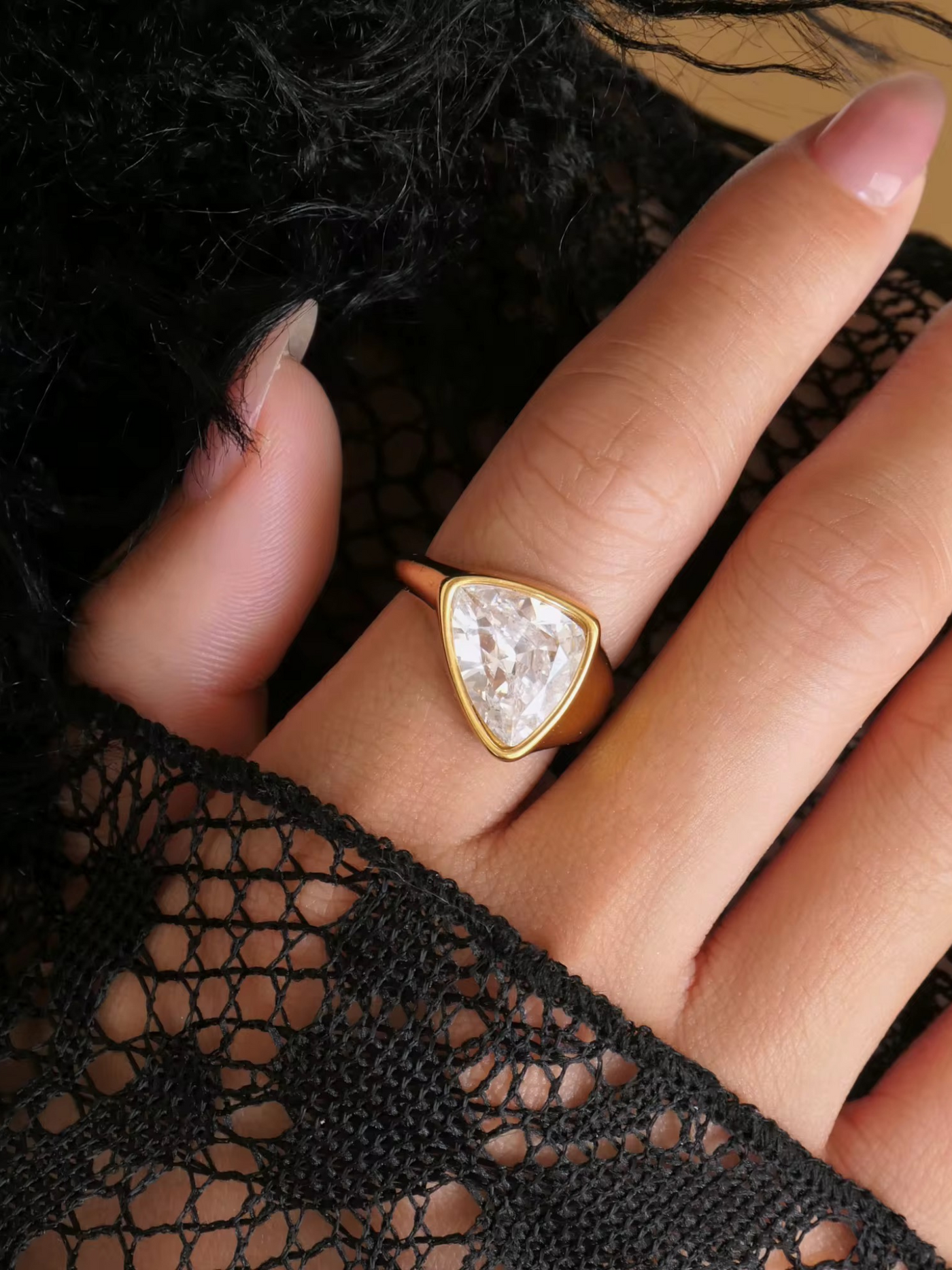 Gold ring with a triangular gemstone on a hand wearing black lace gloves.