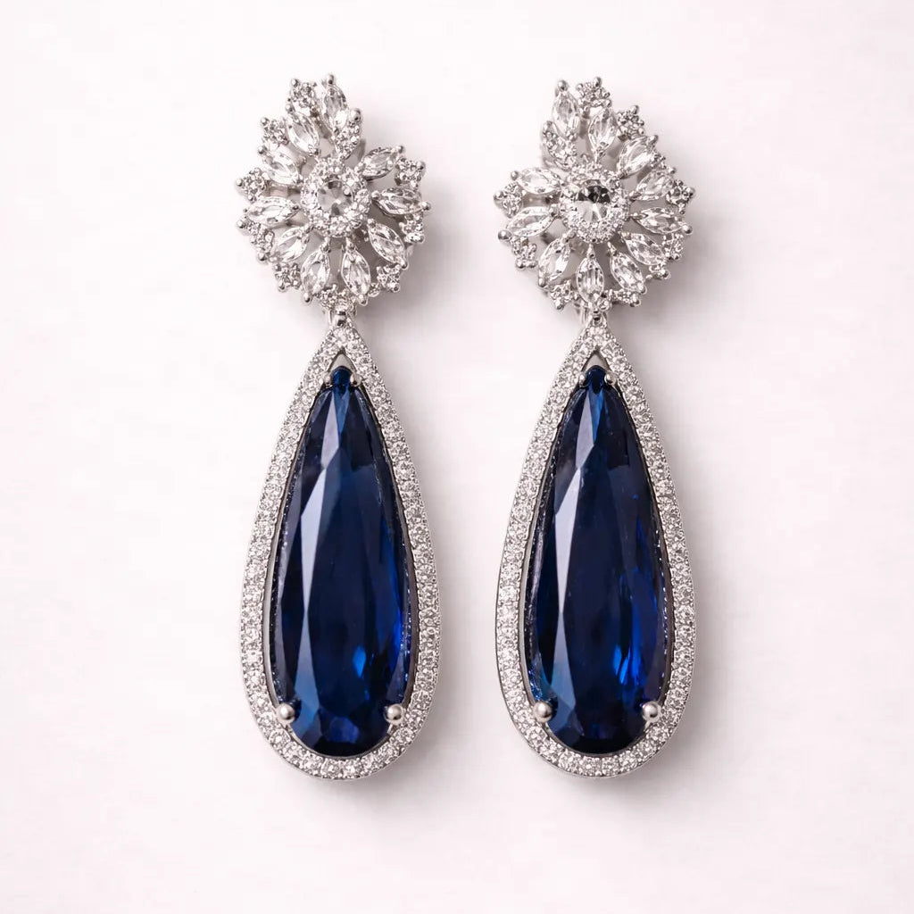 Pair of earrings with blue teardrop stones and silver embellishments on a white background