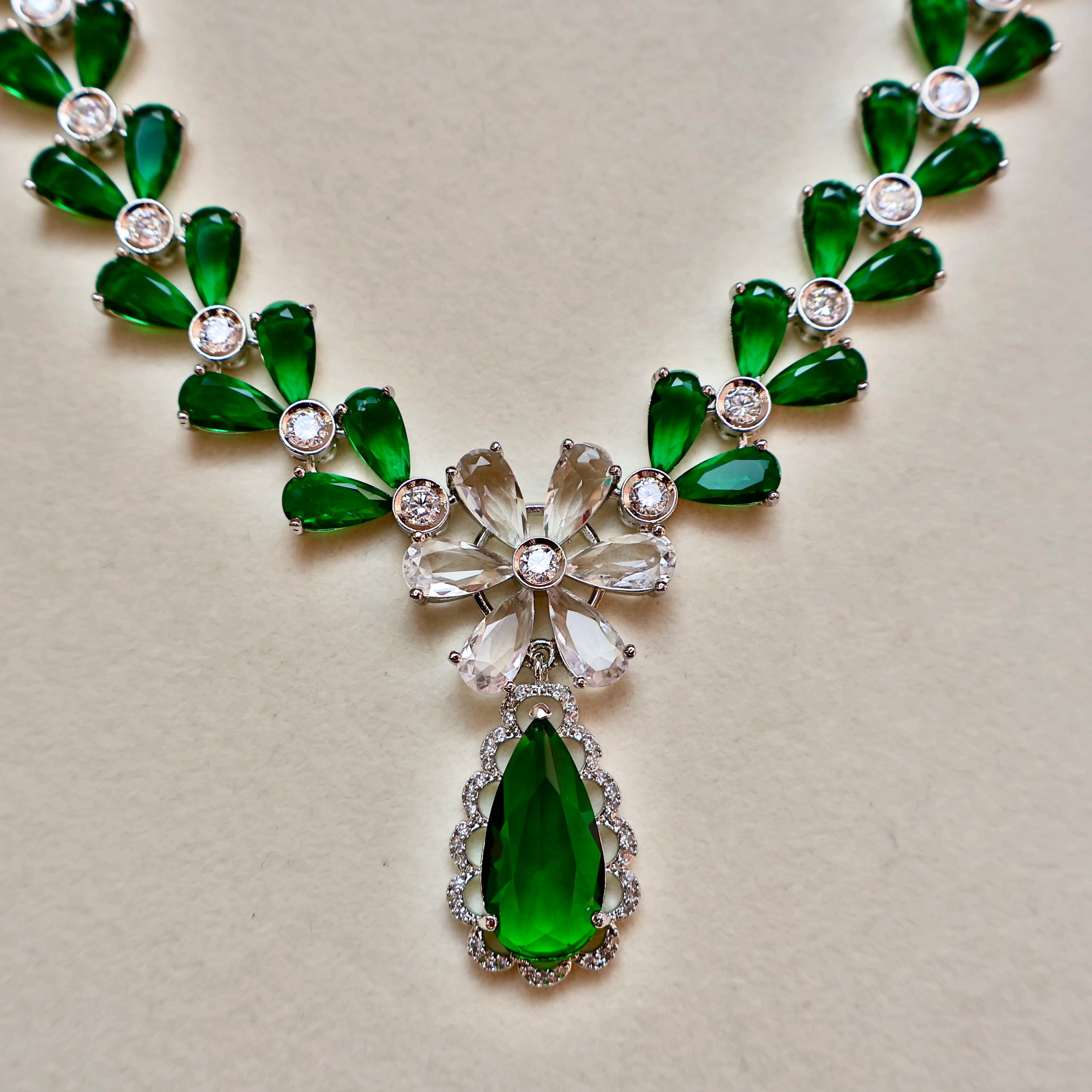 Green gemstone necklace with silver accents on a beige background