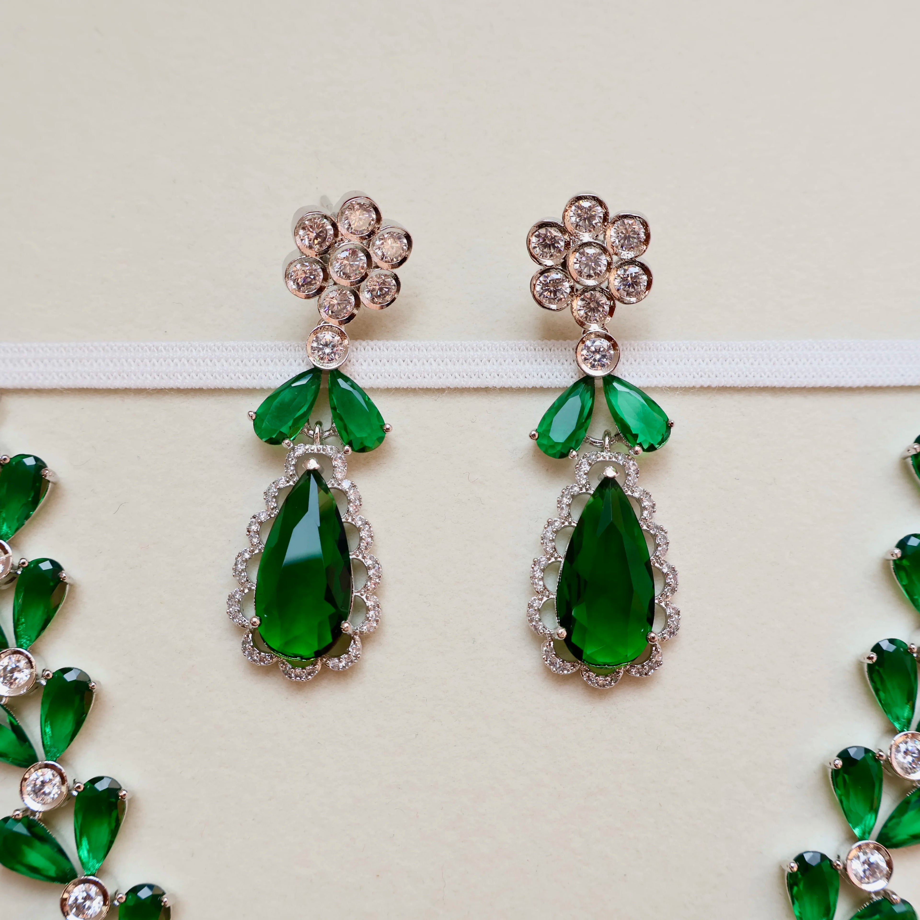 Green teardrop earrings with floral tops on a light background