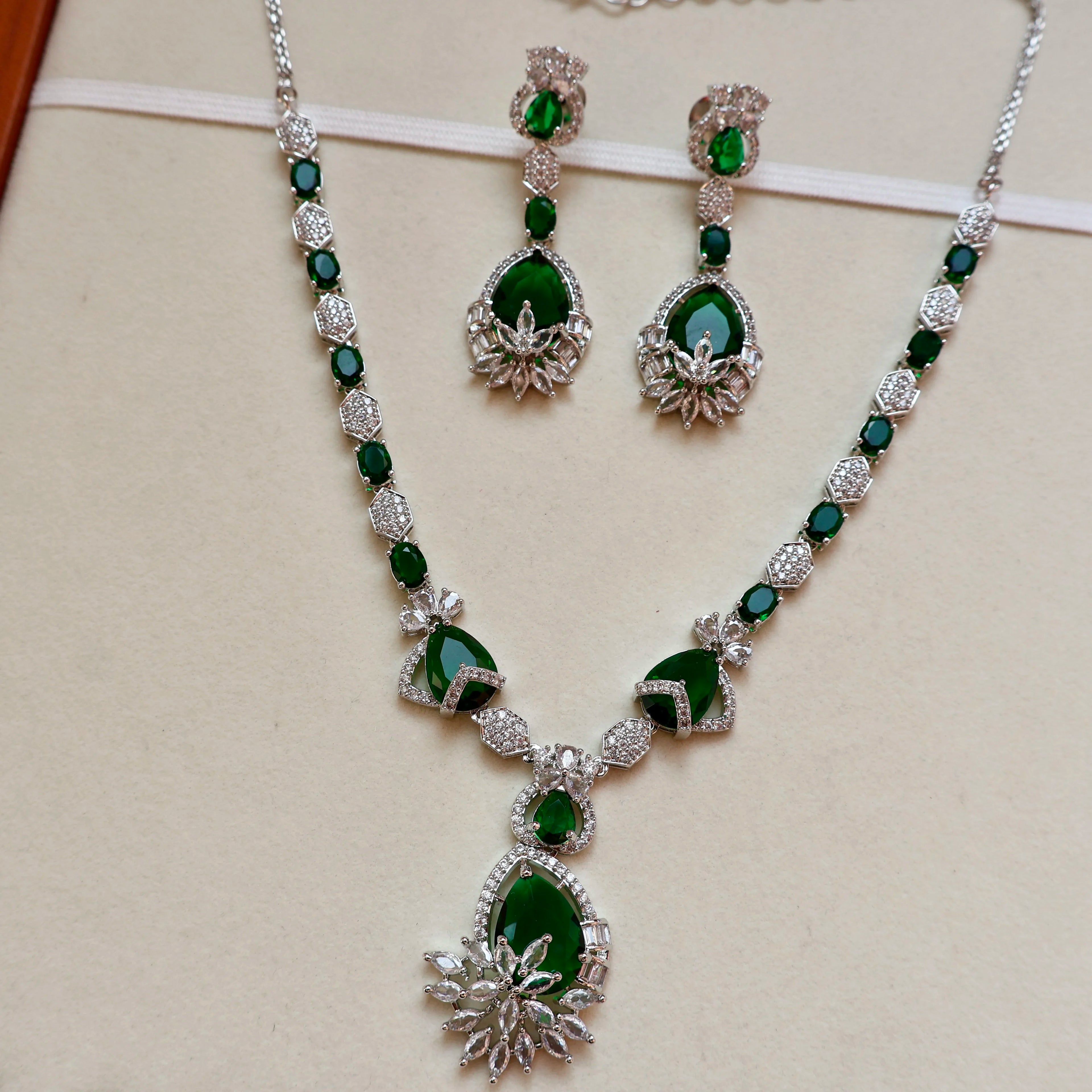 Jewelry set with necklace and earrings featuring green gemstones on a beige background