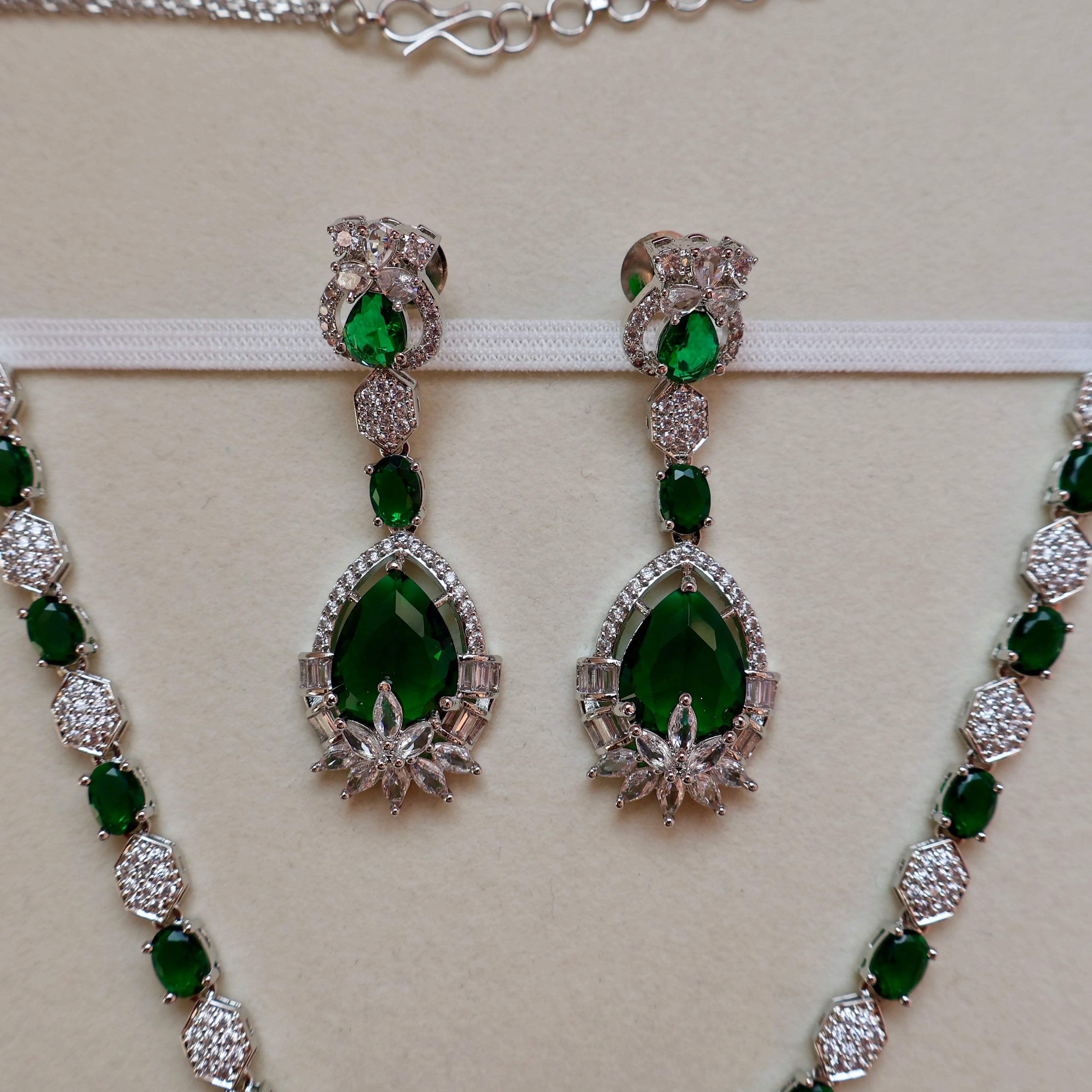 Green gemstone earrings and necklace set on a beige background