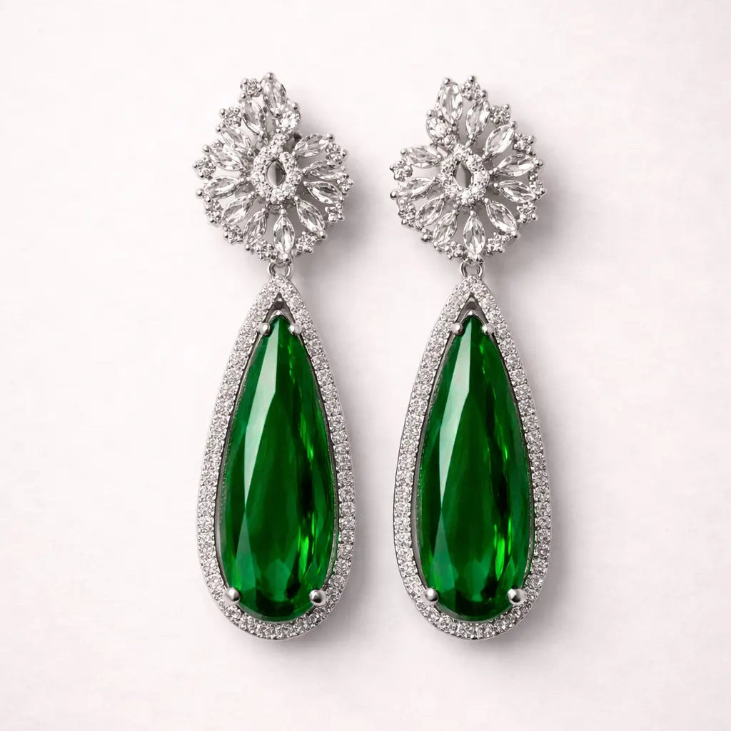 Pair of emerald green teardrop earrings with silver floral tops on a white background