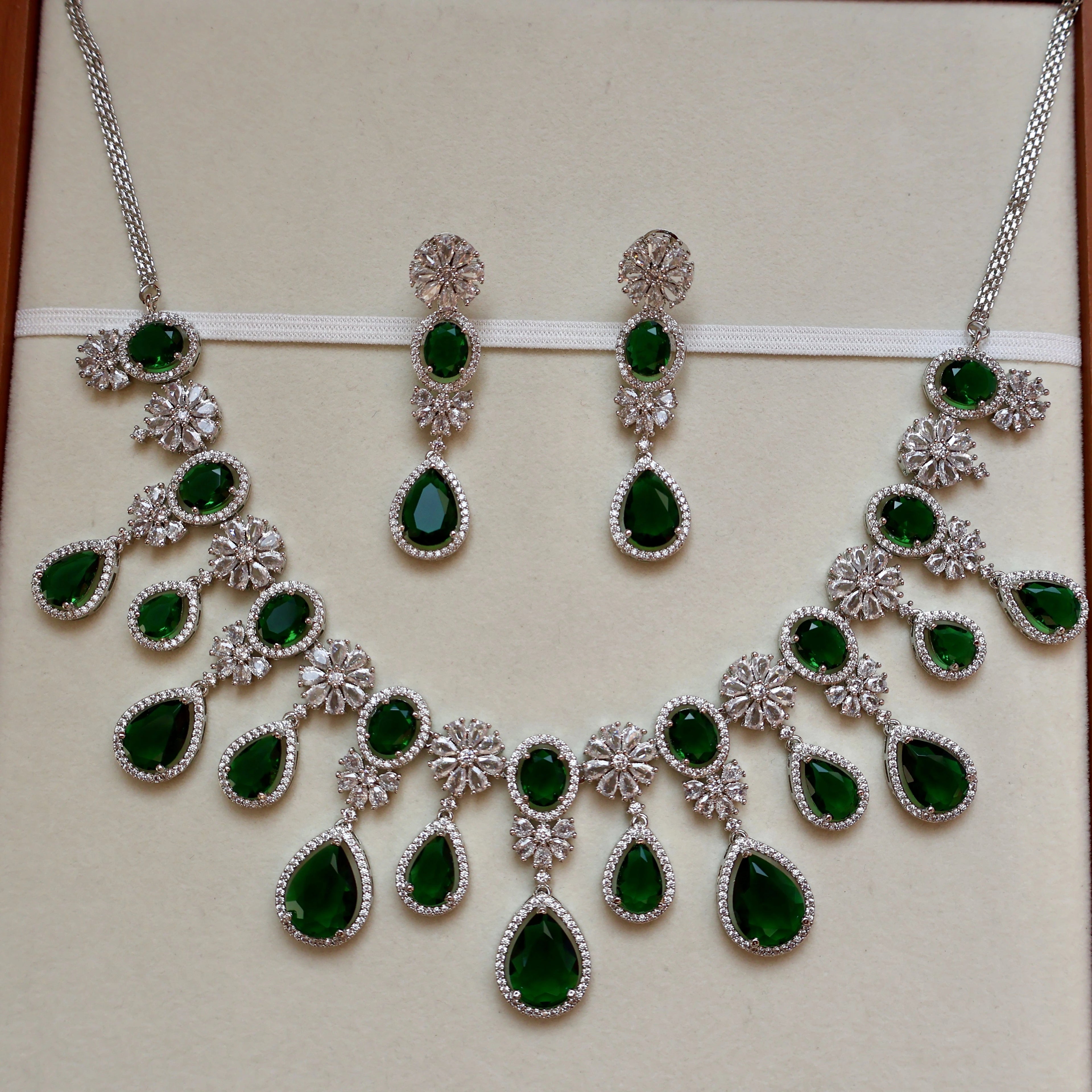 Jewelry set with necklace and earrings featuring green gemstones on a beige background