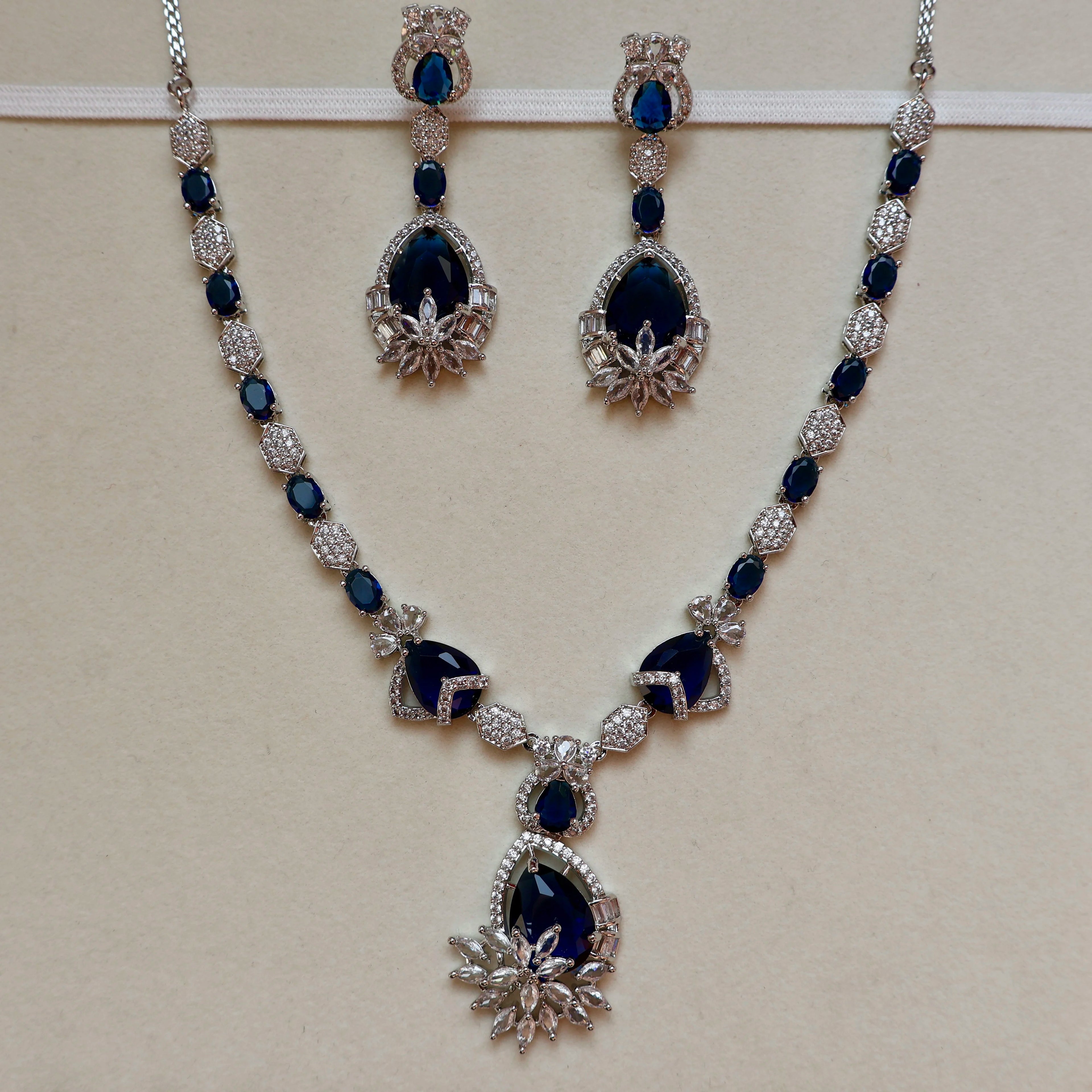 Jewelry set with necklace and earrings featuring blue stones and silver accents on a beige background.