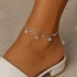 Silver anklet with charms on a person's ankle against a neutral background