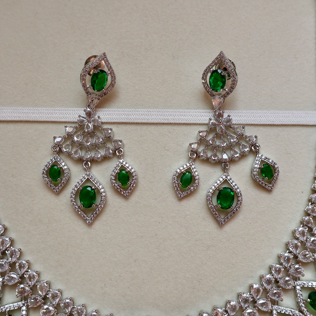 Pair of silver earrings with green gemstones on a beige background
