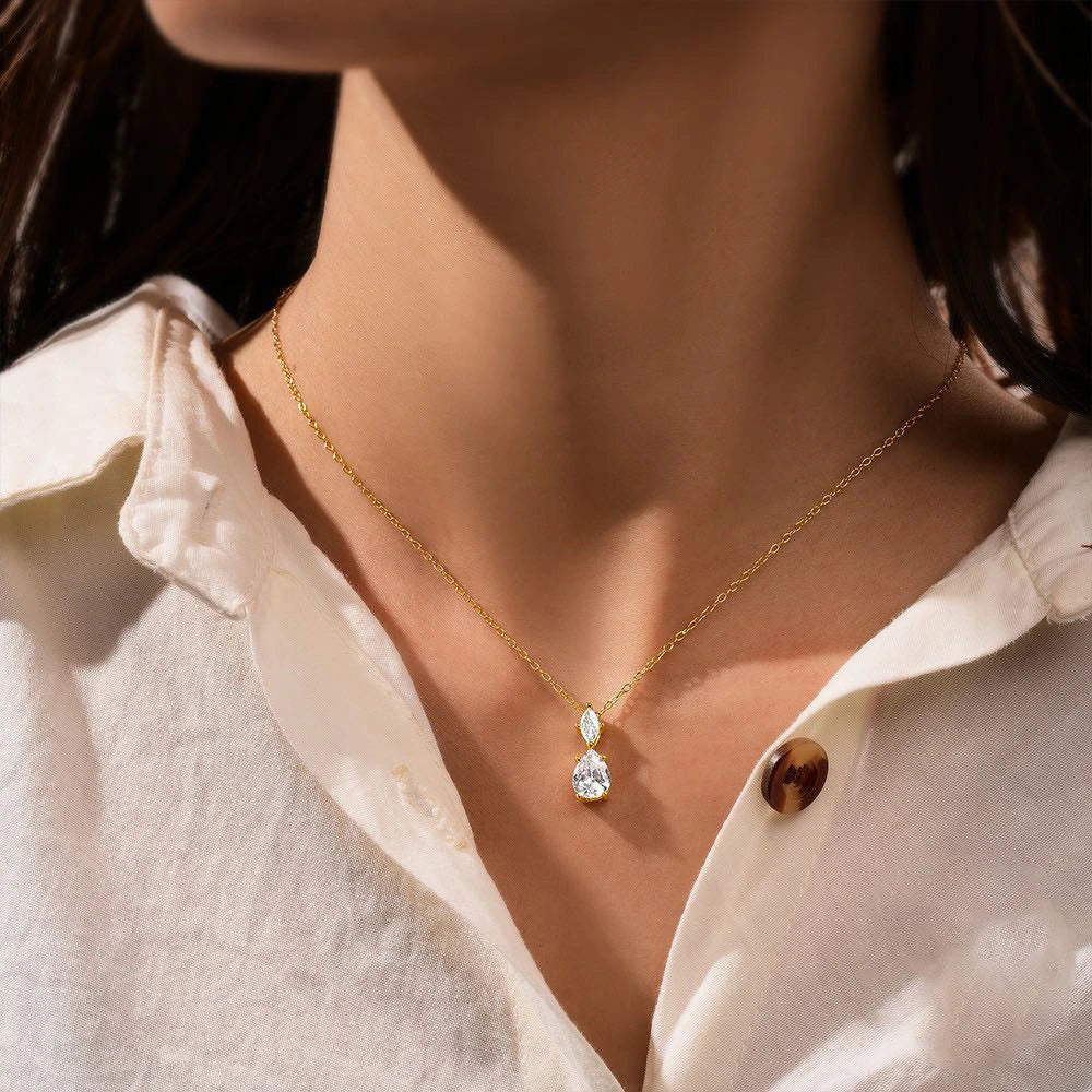 Gold necklace with a teardrop-shaped pendant worn by a person in a white shirt.