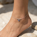 Silver anklet with a blue charm on a foot against a natural background