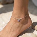 Silver anklet with a blue charm on a foot against a natural background
