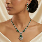 Close-up of a woman wearing an emerald and diamond necklace and earrings on a beige background