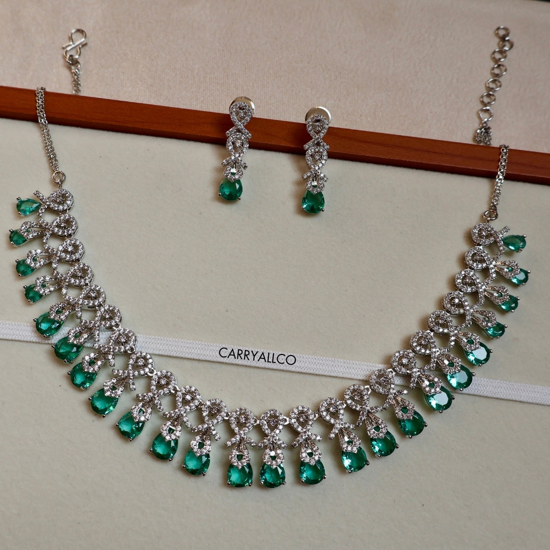 Jewelry set with necklace and earrings featuring green gemstones on a beige background.
