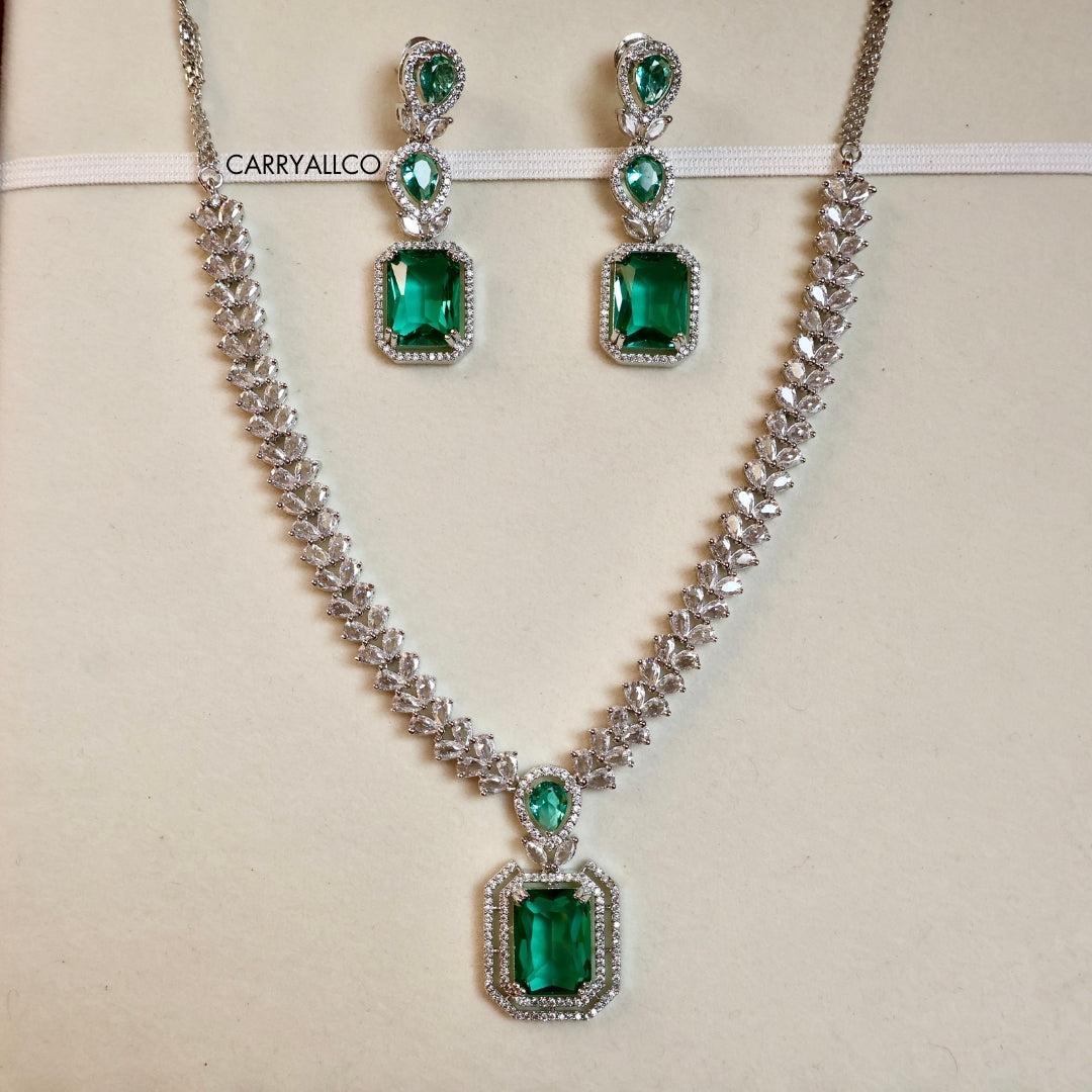 Jewelry set with emerald green gemstones and silver accents on a beige background.