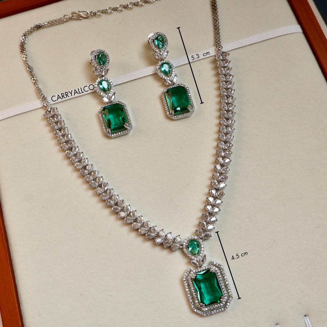 Jewelry set with emerald green stones and silver chains on a beige background