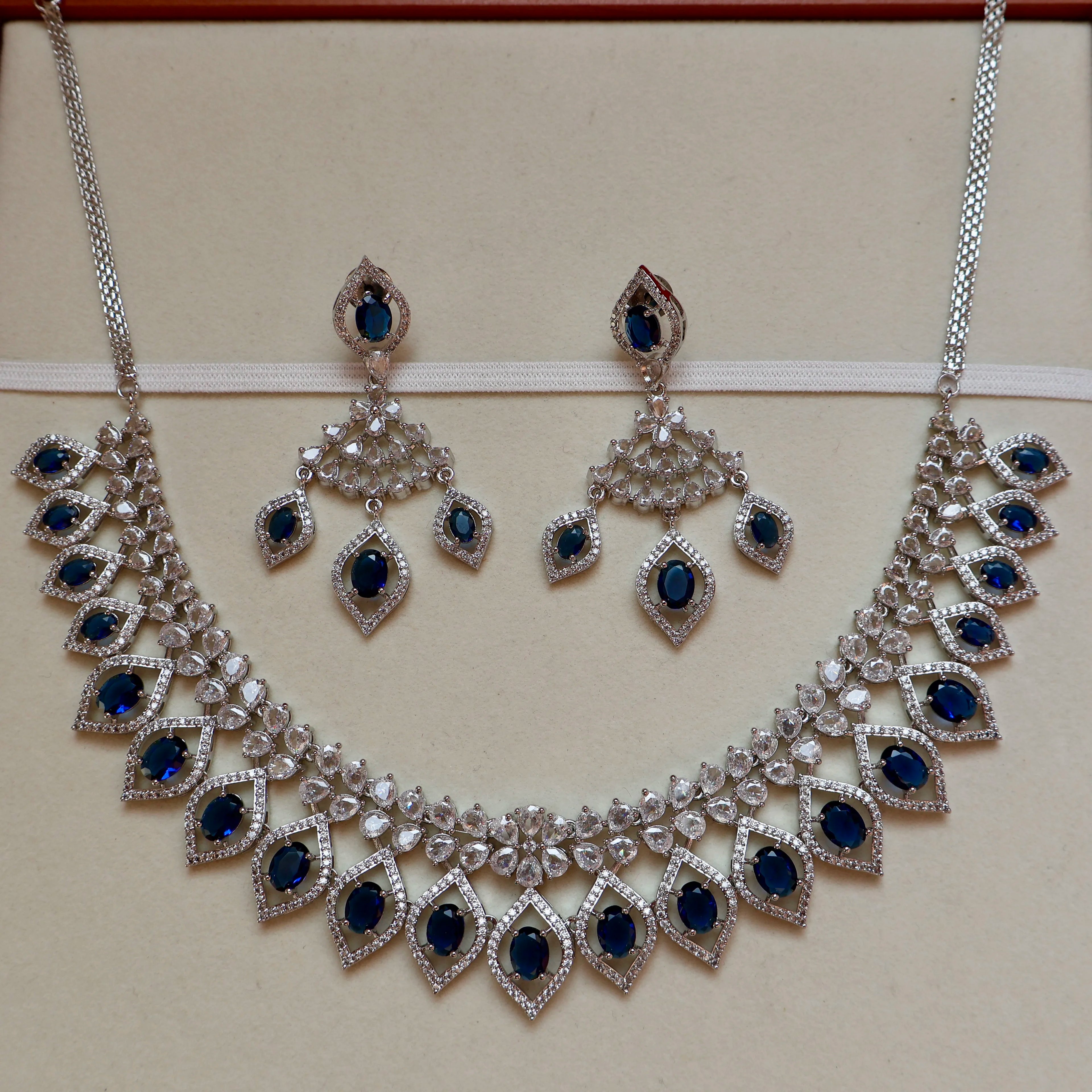 Silver necklace with blue gemstones and matching earrings on a beige background