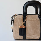 Beige handbag with black handle and gold chain detail on a light gray background