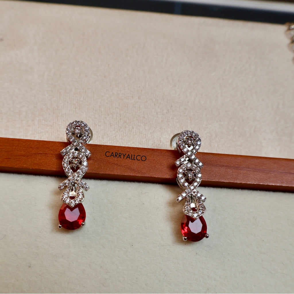 Pair of red gemstone earrings with silver detailing on a wooden stick with 'CARRYALCO' branding.