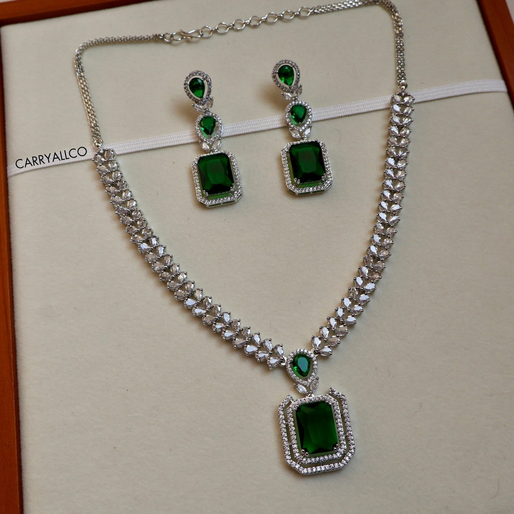 Jewelry set with necklace and earrings featuring green gemstones on a beige background.